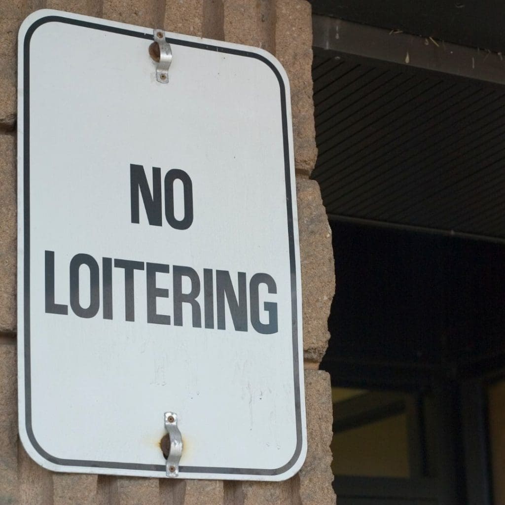 A close-up image of a "No Loitering" sign mounted on a textured brick wall outside a building.