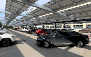 Car dealership lot with multiple vehicles parked under a solar panel-covered structure, highlighting modern security and sustainability measures in automotive retail spaces.