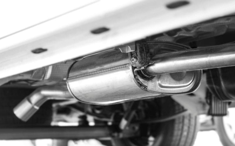 Close-up of a catalytic converter under a vehicle, a common target for thieves due to valuable metals like platinum, palladium, and rhodium. EyeQ Monitoring's AI-powered surveillance and real-time deterrence strategies help dealerships prevent catalytic converter theft.