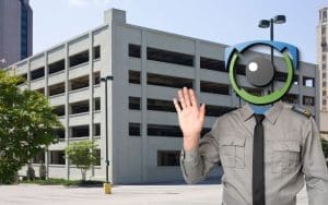 A virtual security guard with an AI-powered surveillance camera for a head stands in front of a multi-level parking garage, symbolizing the power of live video monitoring for parking garage security. AI-driven remote surveillance solutions help prevent theft, vandalism, and unauthorized access while reducing security costs for commercial properties.