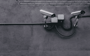 Two wall-mounted security cameras on a dark concrete building exterior, positioned at different angles for broader surveillance coverage.