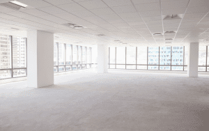 Bright, empty commercial office space with large windows, white walls, and overhead lighting, representing a vacant property at risk without proper security measures.