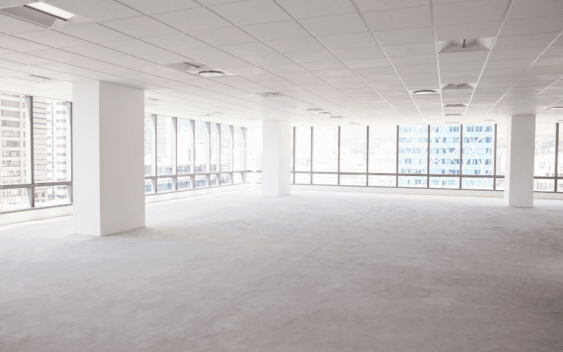 Bright, empty commercial office space with large windows, white walls, and overhead lighting, representing a vacant property at risk without proper security measures.