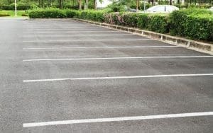 Empty outdoor parking lot viewed from above, with painted white lines and faint shadow cast across the pavement.
