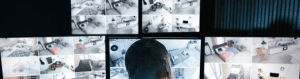 Security operations personnel monitoring multiple live CCTV camera feeds on large screens, showing various indoor locations in real time.