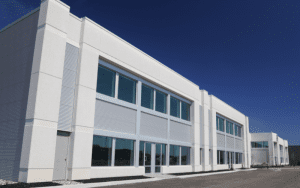 Modern white commercial building with large windows under a clear blue sky, representing professional properties protected by advanced security systems.