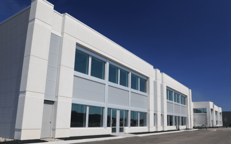 Modern white commercial building with large windows under a clear blue sky, representing professional properties protected by advanced security systems.