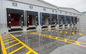 Bird’s-eye view of a commercial loading dock area at night, with trailers backed into bays, security lighting illuminating the perimeter, and surveillance camera coverage zones highlighted in blue.