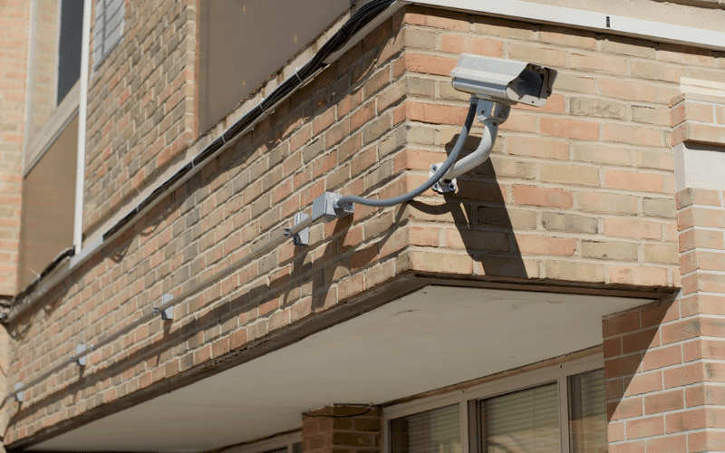 Exterior wall of a multi-family apartment building with a mounted security camera overlooking shared entry points and common areas.