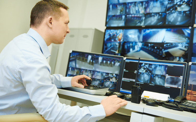 Security professional operating a multi-screen workstation in a control room, actively reviewing live camera feeds as part of a monitoring and surveillance system.