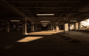 Dimly lit secure parking garage with concrete pillars and overhead lighting, captured during sunset for added shadow contrast