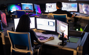 Security operators monitoring multiple live video feeds on computer screens as part of remote security systems for commercial facilities.