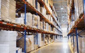Warehouse interior with tall shelves of boxed inventory monitored by warehouse video surveillance systems for security and safety.
